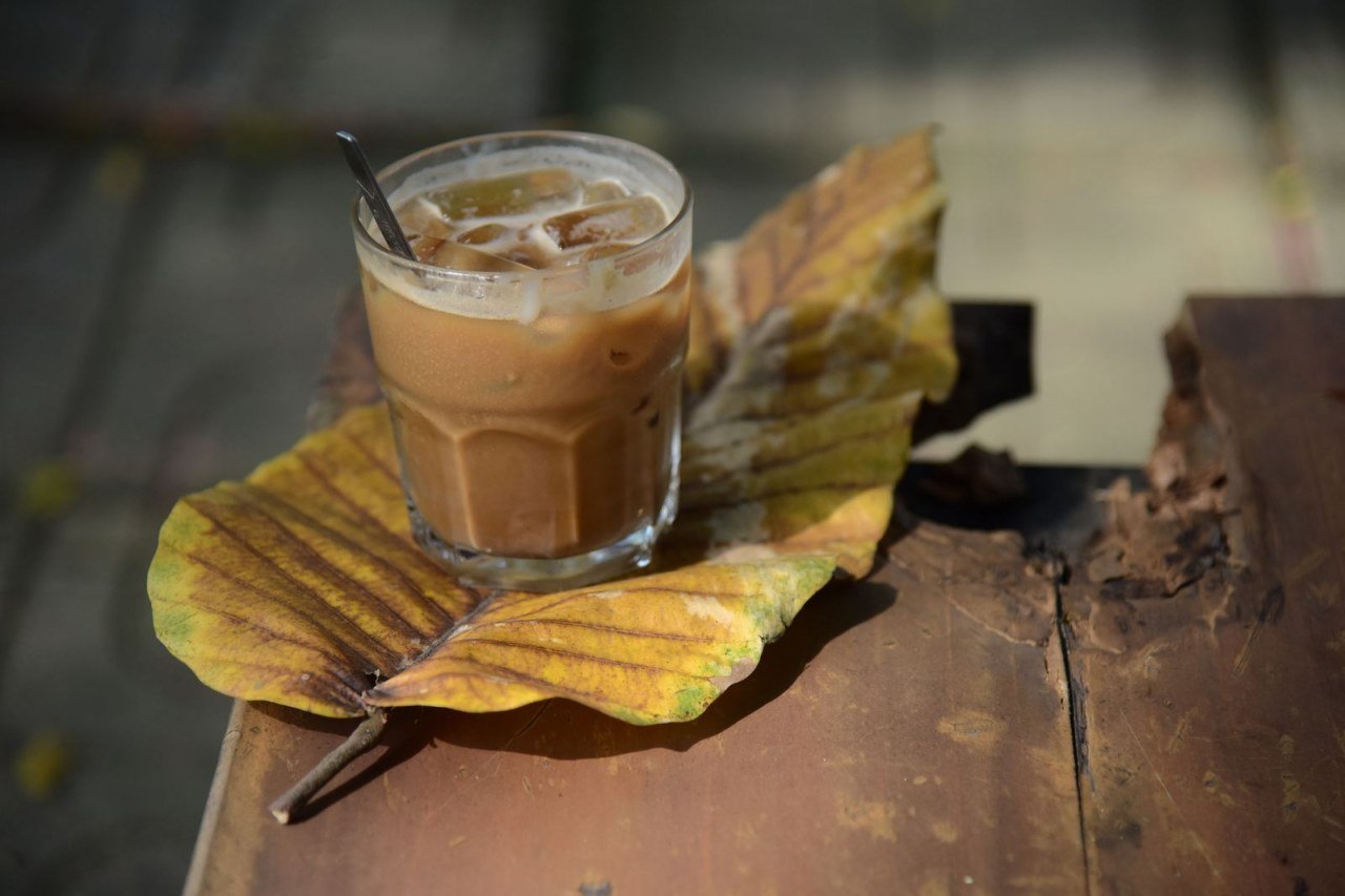 glass of iced coffee on a large autumn leaf on a wooden table