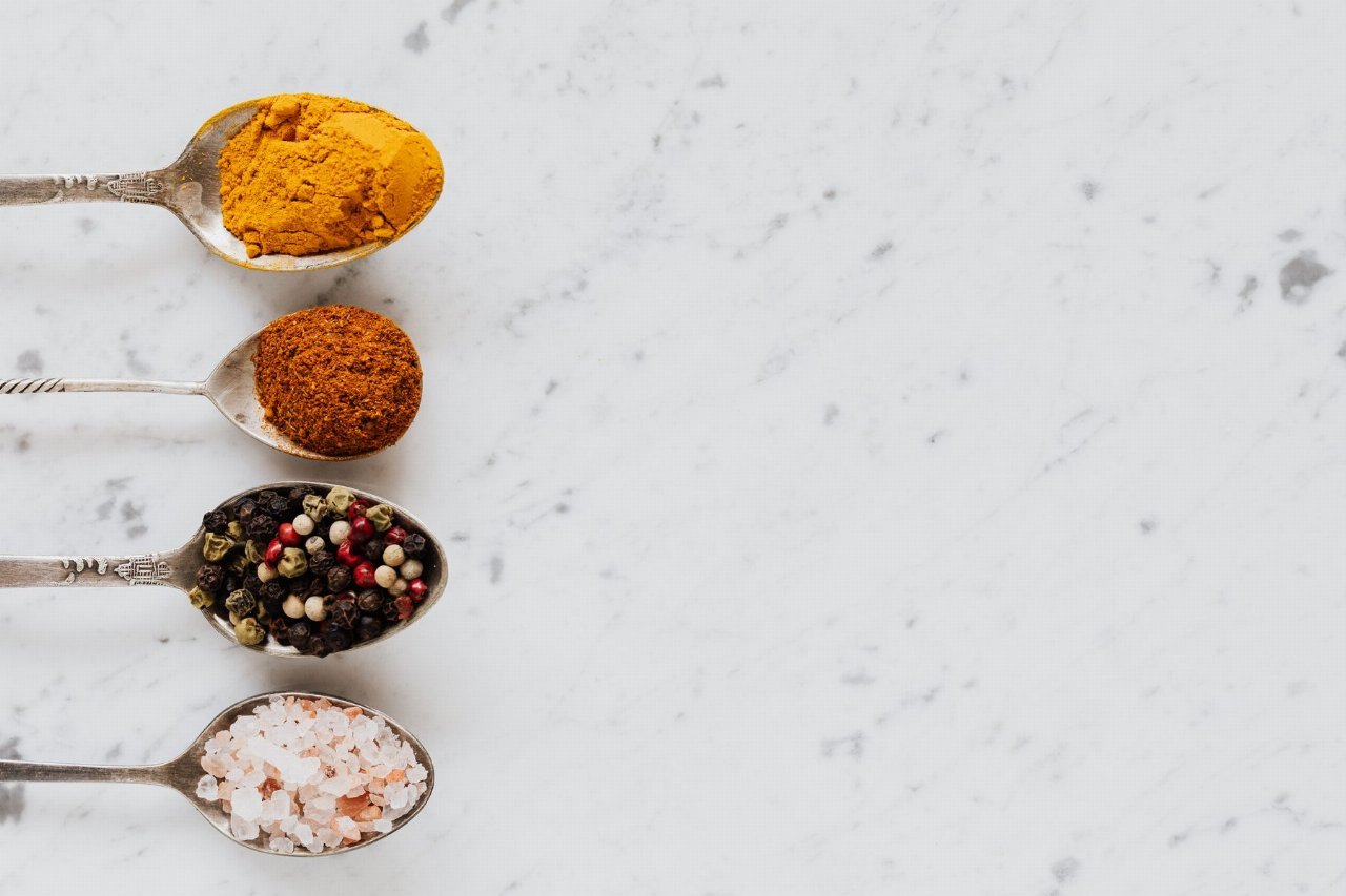turmeric powder and black peppercorns in spoons on a marble table