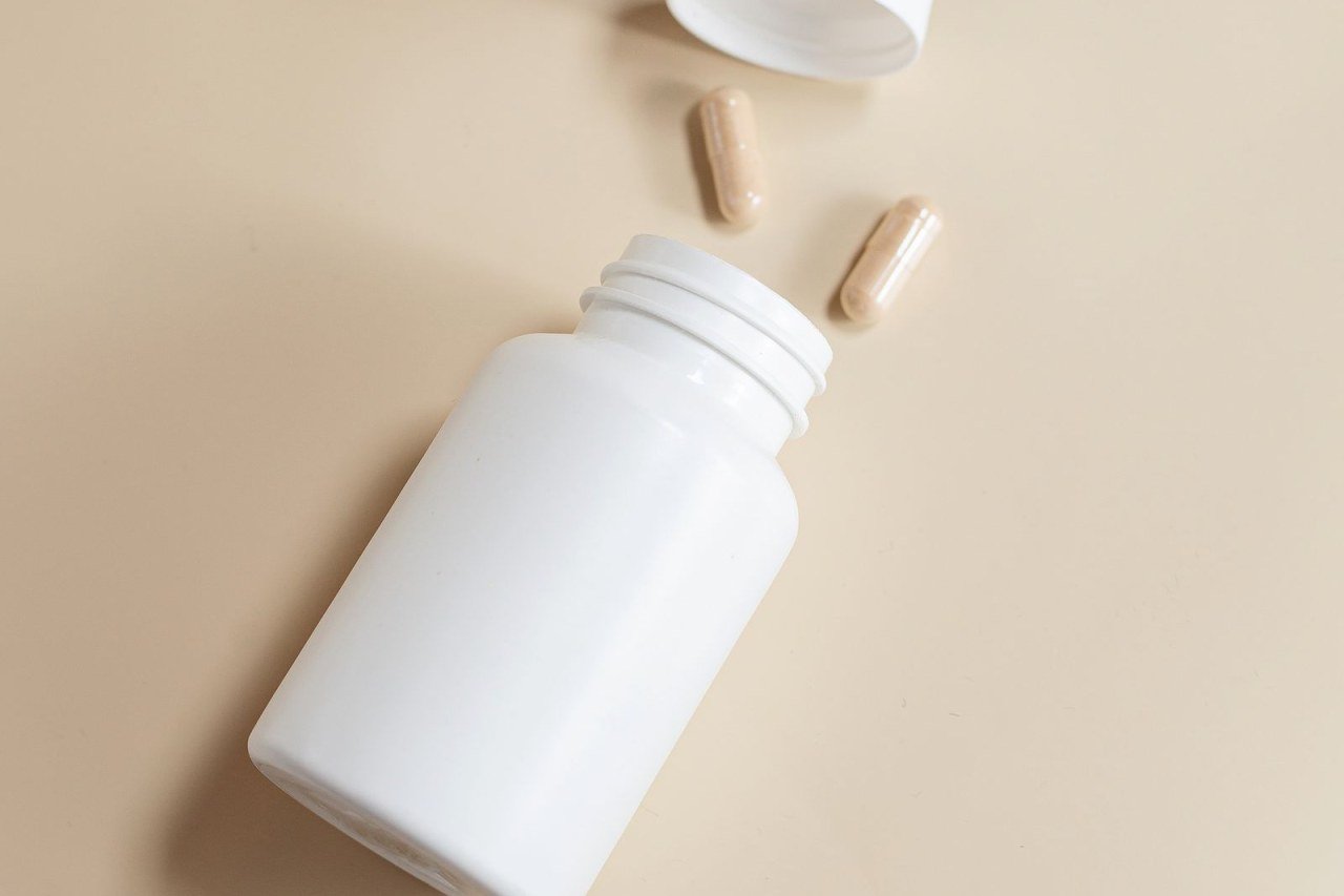 white supplement bottle with capsules spilled on a beige background